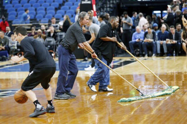 A Portland Trail Blazers player, left, practiced as Target Center workers wipe down the wet basketball floor prior to the NBA basketball game against the Minnesota Timberwolves Monday, March 6, 2017, in Minneapolis. High humidity in Minneapolis and condensation from ice underneath the basketball court for upcoming ice-centered events contributed to the wet floor. (AP Photo/Jim Mone)