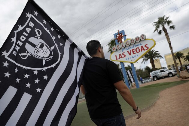 Matt Gutierrez carries a raiders flag by a sign welcoming visitors to Las Vegas, Monday, March 27, 2017, in Las Vegas. NFL team owners approved the move of the Raiders to Las Vegas in a vote at an NFL football annual meeting in Phoenix. (AP Photo/John Locher)