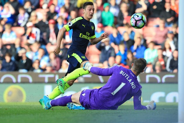Arsenal's German midfielder Mesut Ozil (L) shoots over Stoke City's English goalkeeper Jack Butland to score their second goal during the English Premier League football match between Stoke City and Arsenal at the Bet365 Stadium in Stoke-on-Trent, central England on May 13, 2017. / AFP PHOTO / Lindsey PARNABY / RESTRICTED TO EDITORIAL USE. No use with unauthorized audio, video, data, fixture lists, club/league logos or 'live' services. Online in-match use limited to 75 images, no video emulation. No use in betting, games or single club/league/player publications.  /         (Photo credit should read LINDSEY PARNABY/AFP/Getty Images)