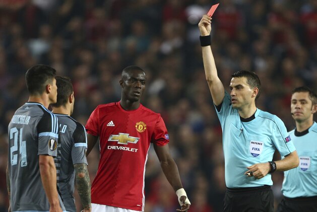 FILE - This is a Thursday, May 11, 2017 file photo of referee Ovidiu Hategan, second right, as he shows the red card and sends off both Manchester United's Eric Bailly, centre,  and Celta's Facundo Roncaglia, left, during the Europa League semifinal second leg soccer match between Manchester United and Celta Vigo at Old Trafford in Manchester, England.  UEFA said Monday July 24, 2017 that Manchester United defender Eric Bailly is suspended from the Super Cup game against Real Madrid and a Champions League group-stage game. UEFA's disciplinary panel imposed a three-match ban for violent conduct after Bailly was sent off late in Man United's Europa League semifinal, second-leg game against Celta Vigo in May. (AP Photo/Dave Thompson/File)