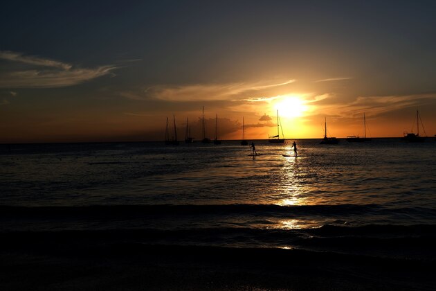 Two tourists sail on paddle board on the water along a beach as the sun sets in Bridgetown, Barbados, on March 24, 2017. / AFP PHOTO / Jewel SAMAD        (Photo credit should read JEWEL SAMAD/AFP/Getty Images)