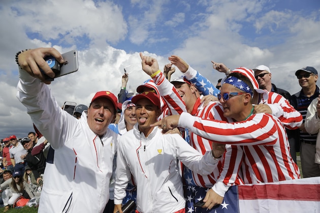 The United States' Phil Mickelson, left and Rickie Fowler take a selfie with fans on the eighth hole during the four-ball golf matches on the third day of the Presidents Cup at Liberty National Golf Club in Jersey City, N.J., Saturday, Sept. 30, 2017. (AP Photo/Julio Cortez)