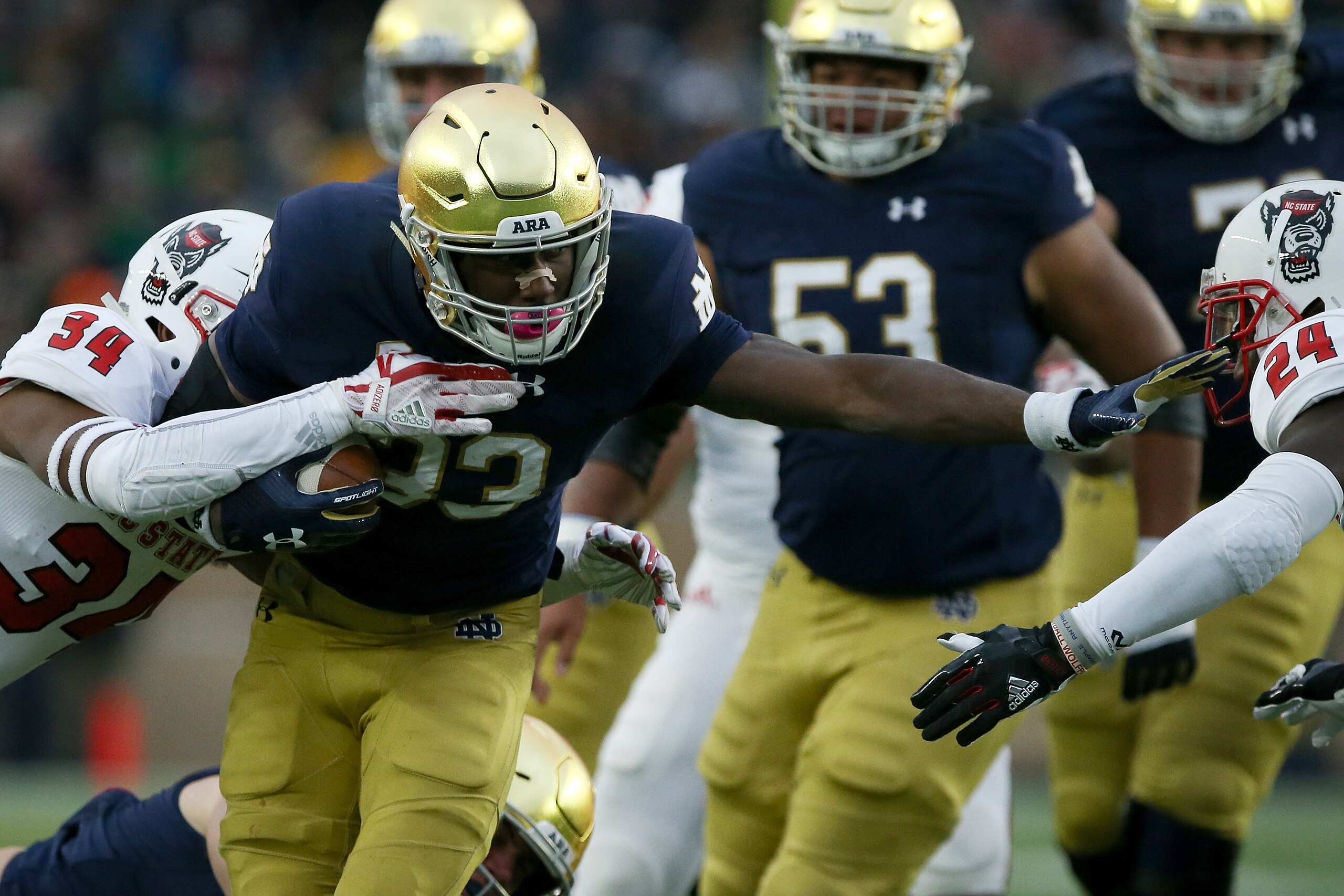 SOUTH BEND, IN - OCTOBER 28:  Josh Adams #33 of the Notre Dame Fighting Irish runs with the ball while being tackled by Tim Kidd-Glass #34 and Shawn Boone #24 of the North Carolina State Wolfpack in the second quarter at Notre Dame Stadium on October 28, 2017 in South Bend, Indiana. (Photo by Dylan Buell/Getty Images)