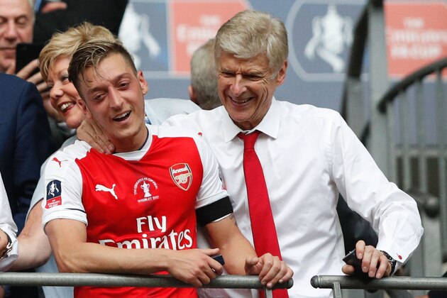 Arsenal's French manager Arsene Wenger (R) and Arsenal's German midfielder Mesut Ozil smile as Arsenal players celebrate their victory over Chelsea in the English FA Cup final football match between Arsenal and Chelsea at Wembley stadium in London on May 27, 2017.
Aaron Ramsey scored a 79th-minute header to earn Arsenal a stunning 2-1 win over Double-chasing Chelsea on Saturday and deliver embattled manager Arsene Wenger a record seventh FA Cup. / AFP PHOTO / Adrian DENNIS / NOT FOR MARKETING OR ADVERTISING USE / RESTRICTED TO EDITORIAL USE        (Photo credit should read ADRIAN DENNIS/AFP/Getty Images)