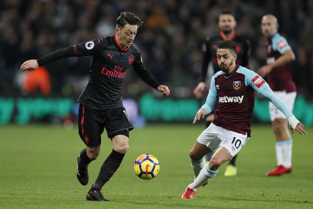 Arsenal's Mesut Ozil, left, competes for the ball with West Ham's Manuel Lanzini during the English Premier League soccer match between West Ham and Arsenal at the London stadium in London, Wednesday, Dec. 13, 2017. (AP Photo/Kirsty Wigglesworth)