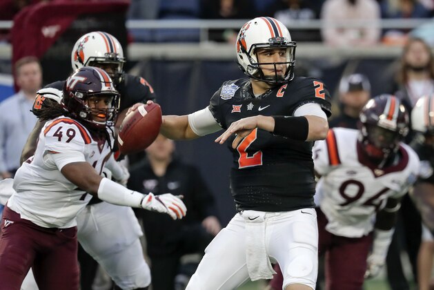 Oklahoma State quarterback Mason Rudolph (2) throws a pass as he is pressured by Virginia Tech linebacker Tremaine Edmunds (49) and defensive end Trevon Hill (94) during the first half of the Camping World Bowl NCAA college football game Thursday, Dec. 28, 2017, in Orlando, Fla. (AP Photo/John Raoux)