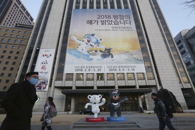 People pass a banner promoting the upcoming 2018 Pyeongchang Winter Olympic as official mascots, a white tiger