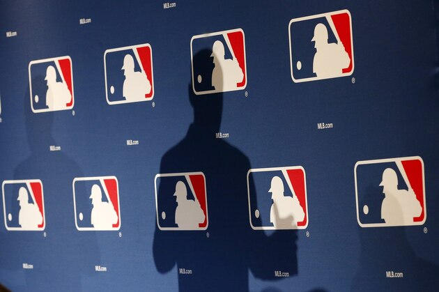 FILE - In this Monday, Feb. 23, 2015 file photo, the shadow of MLB Commissioner Rob Manfred is projected on an MLB logo backdrop in Phoenix. Major league teams steeply increased the money spent on young players in 2015, but the overall percentage of revenue devoted to players has remained relatively stable for a decade. (AP Photo/Ross D. Franklin)