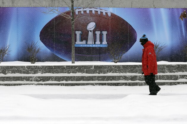 Snow falls as a man passes signage for the NFL Super Bowl 52 football game at U.S. Bank Stadium, Saturday, Feb. 3, 2018, in Minneapolis. The Philadelphia Eagles are scheduled to face the New England Patriots Sunday. (AP Photo/Eric Gay)
