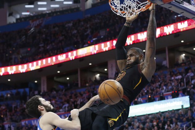 Cleveland Cavaliers forward LeBron James hangs from the basket after dunking in front of Oklahoma City Thunder guard Alex Abrines during the first half of an NBA basketball game in Oklahoma City, Tuesday, Feb. 13, 2018. (AP Photo/Sue Ogrocki)