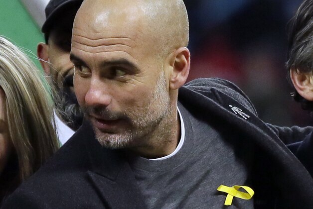 In this photo taken Sunday, Feb. 25, 2018, Manchester City's manager Pep Guardiola wears a yellow ribbon on his jumper during the celebrations after his side won the English League Cup Final between Arsenal and Manchester City 0-3, at Wembley stadium in London.  Guardiola defied an English Football Association charge for promoting a political message by continuing to wear a yellow ribbon, seen as criticism of the imprisonment of pro-independence Catalan politicians in Spain. (AP Photo/Tim Ireland)