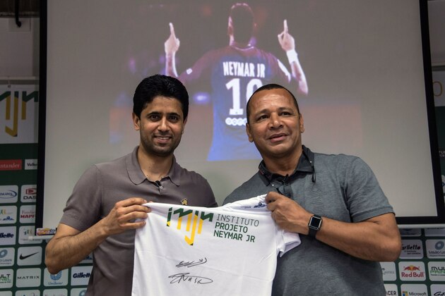 French football team Paris Saint-Germain's (PSG) Qatari president Nasser Al-Khelaifi (L) and Neymar Santos, father of Brazilian superstar and PSG's footballer Neymar Junior, pose for pictures holding a t-shirt of Neymar Junior Institute project, during a press conference, in Praia Grande, Sao Paulo, Brazil on March 13, 2018. 
Nasser Al-Khelaifi arrived in Brazil to visit the world's most expensive player, Neymar, who broke a bone in his right foot on February 25 and faces weeks of recuperation following surgery. The visit also takes place amid rumors swirling about the striker's intention to quit PSG. / AFP PHOTO / NELSON ALMEIDA        (Photo credit should read NELSON ALMEIDA/AFP/Getty Images)