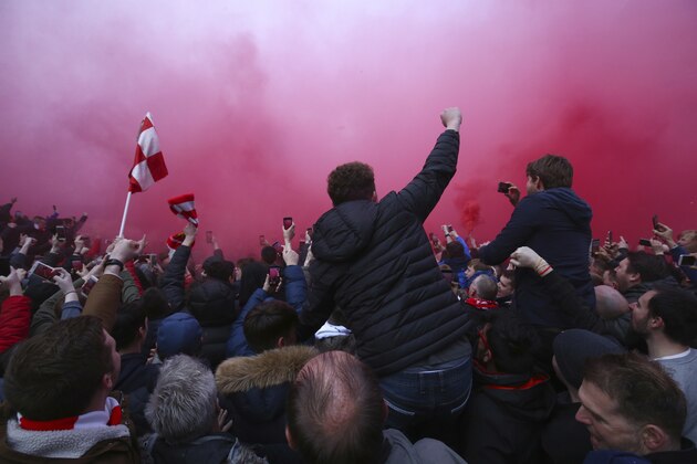 A flare burns as football fans try to see the Manchester City team bus as it arrives ahead of the Champions League quarter final first leg soccer match between Liverpool and Manchester City at Anfield stadium in Liverpool, England, Wednesday, April 4, 2018. (AP Photo/Dave Thompson)