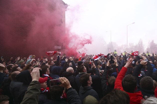 A flare burns as football fans try to see the Manchester City team bus as it arrives ahead of the Champions League quarter final first leg soccer match between Liverpool and Manchester City at Anfield stadium in Liverpool, England, Wednesday, April 4, 2018. (AP Photo/Dave Thompson)