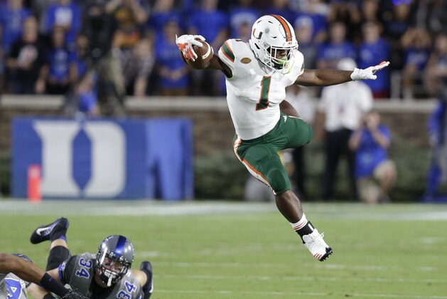 Miami's Mark Walton (1) jumps over Duke's Ben Humphreys and Bryon Fields Jr. during the first half of an NCAA college football game in Durham, N.C., Friday, Sept. 29, 2017. (AP Photo/Gerry Broome)