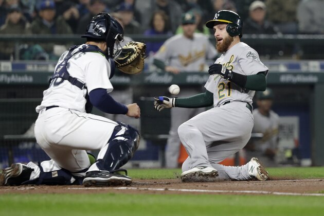 In a play that was later called back following a review, Seattle Mariners catcher David Freitas, left, loses the ball as Oakland Athletics' Jonathan Lucroy is apparently safe at home in the third inning during a baseball game Saturday, April 14, 2018, in Seattle. After a review, Lucroy was sent back to third base and teammate Marcus Semien was ruled to have hit a ground rule double on the play and sent back to second base. (AP Photo/Elaine Thompson)