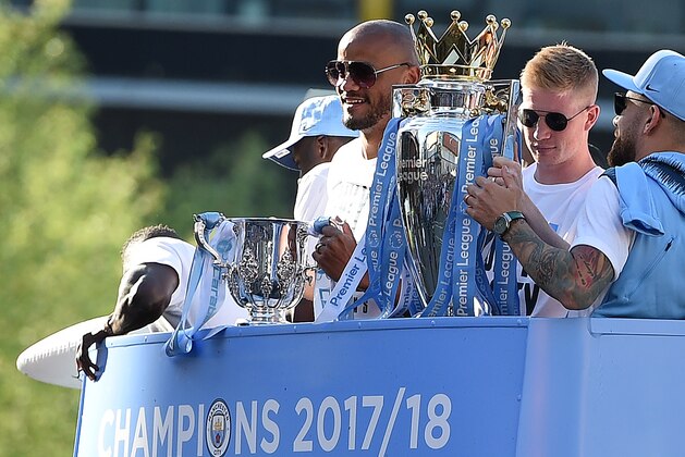 Manchester City's Belgian midfielder Kevin De Bruyne (2R) holds up the Preimer Leagu trophy as Manchester City's Belgian defender Vincent Kompany (C) holds up the English League Cup trophy to fans as the Manchester City team take part in an open-top bus parade through Manchester, northern England on May 14, 2018 to celebrate winning the 2018 Premier League title. - Manchester City set the seal on a record-breaking season by becoming the first side in English top flight history to hit 100 points with victory at Southampton on Sunday. City also added another landmark by winning the league by a record 19 points from local rivals Manchester United. (Photo by Oli SCARFF / AFP)        (Photo credit should read OLI SCARFF/AFP/Getty Images)