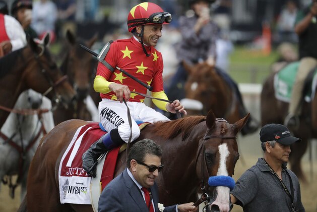 Jockey Mike Smith rides Justify to the winner's circle led by assistant trainer Jimmy Barnes, left, and Carlos Martin after winning the 150th running of the Belmont Stakes horse race and the Triple Crown, Saturday, June 9, 2018, in Elmont, N.Y. (AP Photo/Julio Cortez)