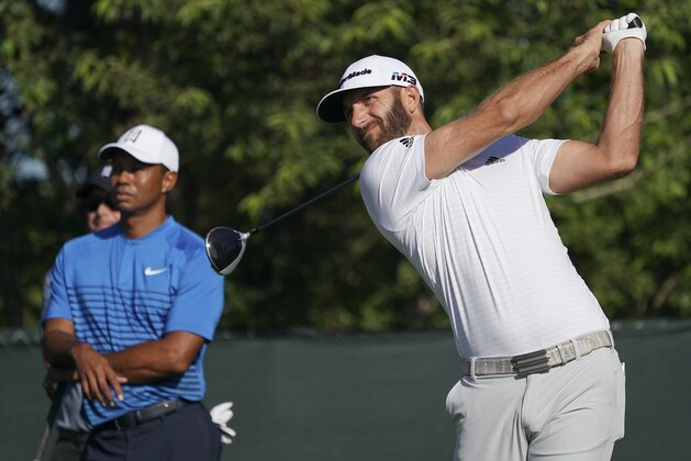 Dustin Johnson hits off the fourth tee as Tiger Woods looks on during a practice round for the U.S. Open Golf Championship, Tuesday, June 12, 2018, in Southampton, N.Y. (AP Photo/Carolyn Kaster)