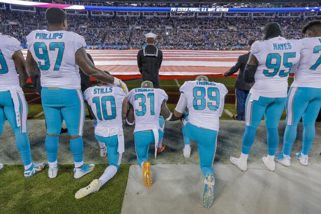 Miami Dolphins' Jordan Phillips (97) stands during the national anthem, but shows support for the protest as he puts an arm on the shoulder of kneeling teammate, Kenny Stills (10), Michael Thomas (31) and Julius Thomas (89) before an NFL football game against the Carolina Panthers in Charlotte, N.C., Monday, Nov. 13, 2017. The Panthers won 45-21. (AP Photo/Bob Leverone)