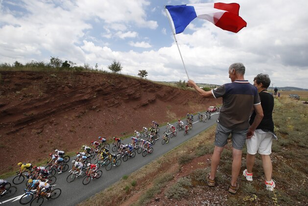 Spectators wave the French flag as the pack with Britain's Geraint Thomas, wearing the overall leader's yellow jersey, bottom left, passes during the fifteenth stage of the Tour de France cycling race over 181.5 kilometers (112.8 miles) with start in Millau and finish in Carcassonne, France, France, Sunday July 22, 2018. (AP Photo/Christophe Ena )