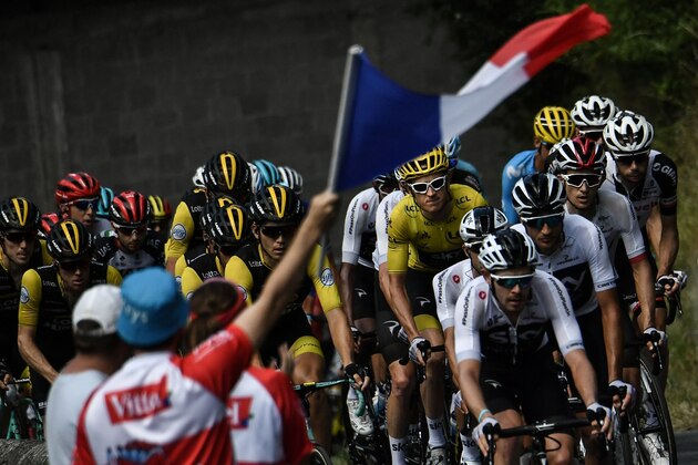 A spectator waves the French flag as Great Britain's Geraint Thomas (C-L), wearing the overall leader's yellow jersey, rides in the pack during the 15th stage of the 105th edition of the Tour de France cycling race, between Millau and Carcassonne on July 22, 2018. (Photo by Marco BERTORELLO / AFP)        (Photo credit should read MARCO BERTORELLO/AFP/Getty Images)