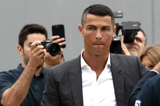 Portuguese footballer Cristiano Ronaldo surrounded by photographs looks on as he greets supporters outside the Juventus medical center at the Alliance stadium in Turin on July 16, 2018. - Cristiano Ronaldo arrived in Turin ahead of his official unveiling as Juventus' superstar summer signing on July 17. (Photo by Isabella Bonotto / AFP)        (Photo credit should read ISABELLA BONOTTO/AFP/Getty Images)