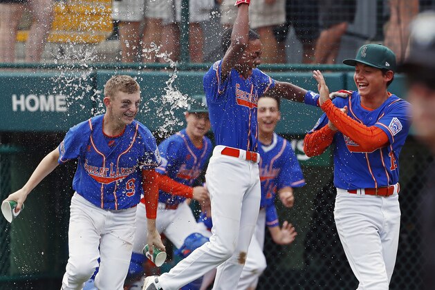 Grosse Pointe Woods, Michigan's Reggie Sharpe, center, gets a water bath from Cameron Schafer (9) as he begins to celebrate with Brennan Hill, right, after hitting a walk off single in the bottom of the sixth inning of an elimination baseball game Des Moines, Iowa in United States pool play at the Little League World Series tournament in South Williamsport, Pa., Monday, Aug. 20, 2018. Michigan won 5-4, eliminating Iowa. (AP Photo/Gene J. Puskar)