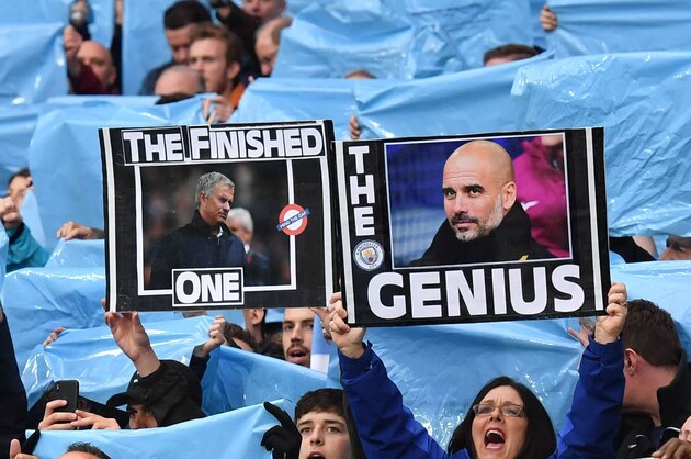 Manchester City fans hold up placards showing the faces of Manchester City's Spanish manager Pep Guardiola (R) and Manchester United's Portuguese manager Jose Mourinho (L) during the English Premier League football match between Manchester City and Manchester United at the Etihad Stadium in Manchester, north west England, on April 7, 2018. / AFP PHOTO / Ben STANSALL / RESTRICTED TO EDITORIAL USE. No use with unauthorized audio, video, data, fixture lists, club/league logos or 'live' services. Online in-match use limited to 75 images, no video emulation. No use in betting, games or single club/league/player publications.  /         (Photo credit should read BEN STANSALL/AFP/Getty Images)