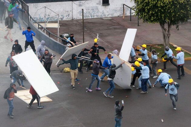 In this photo provided by the Andina government news agency, Alianza Lima club soccer fans, left, fight with members of an evangelical church, yellow helmets at right, outside the soccer club's stadium in Lima, Peru, Monday, Sept. 10, 2018. The two groups clashed outside the stadium over who has the right to use the area surrounding the sports venue, after the religious group arrived early in the morning and started removing the team's logos from the parking area. (Norman Cordova/Andina News Agency via AP)
