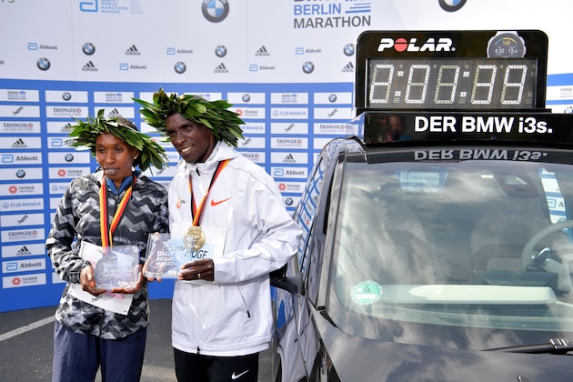 Winner Kenya's Eliud Kipchoge (R) and women's winner Kenya's Gladys Cherono pose with their trophies and medals next to a clock displaying Kipchoge's winning time setting a new record after the Berlin Marathon on September 16, 2018 in Berlin. (Photo by John MACDOUGALL / AFP)        (Photo credit should read JOHN MACDOUGALL/AFP/Getty Images)