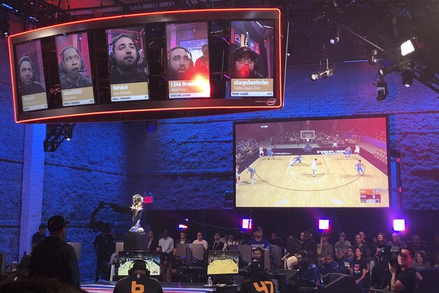 Heat Check Gaming players are seen on the screens above their seats while action from their game against Knicks Gaming is shown on another screen, Saturday, Aug. 25, 2018, in New York. The Knicks sweep the Heat to win the inaugural NBA 2K Finals. (AP Photo/Brian Mahoney)