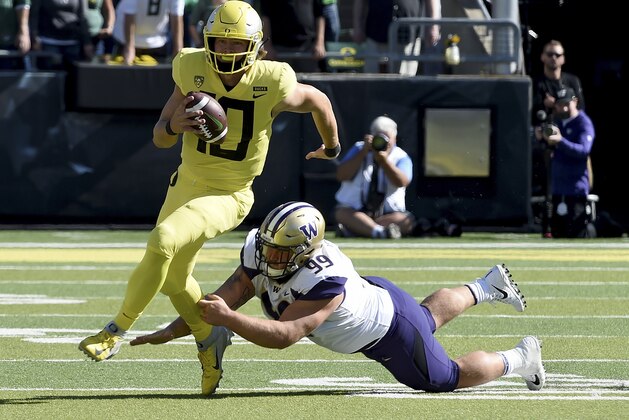 EUGENE, OR - OCTOBER 13:  Quarterback Justin Herbert #10 of the Oregon Ducks scrambles against defensive lineman Greg Gaines #99 of the Washington Huskies in the first half of the game at Autzen Stadium on October 13, 2018 in Eugene, Oregon.  (Photo by Steve Dykes/Getty Images)