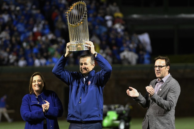 Tom Ricketts, center, with Laura Ricketts and Todd Ricketts, hoists the 2016 World Series Championship trophy before a baseball game between the Chicago Cubs and the Los Angeles Dodgers on a home opening day, Monday, April 10, 2017, in Chicago. (AP Photo/David Banks)
