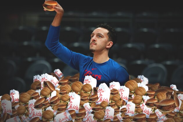 Philadelphia 76ers center Joel Embiid (21) eats a sandwich as he receives treatment from a trainer on the court before play against the Miami Heat in Game 4 of a first-round NBA basketball playoff series, Saturday, April 21, 2018, in Miami. (AP Photo/Joe Skipper)