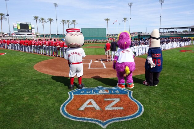 Cincinnati Reds mascot Mr. Redlegs, left, Cleveland Indians mascot Slider, and Goodyear Ballpark mascot Zizzy pause along with player from the Reds and the Indians for the national anthem prior to a Cactus League baseball game Tuesday, March 1, 2016, in Goodyear, Ariz.  The Reds defeated the Indians 6-5. (AP Photo/Ross D. Franklin)