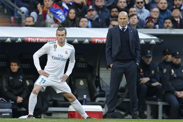 Real Madrid's Gareth Bale stretches next to Real Madrid's head coach Zinedine Zidane while waiting to come on as substitute during a Spanish La Liga soccer match between Real Madrid and Barcelona at the Santiago Bernabeu stadium in Madrid, Spain, Saturday, Dec. 23, 2017. (AP Photo/Paul White)