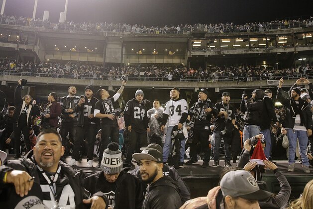 Fans stand on a dugout at Oakland Alameda County Coliseum after an NFL football game between the Oakland Raiders and the Denver Broncos in Oakland, Calif., Monday, Dec. 24, 2018. (AP Photo/John Hefti)
