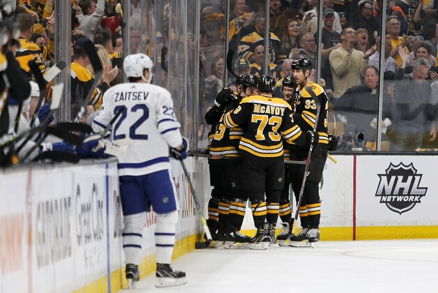 Boston Bruins players surround teammate Charlie Coyle after he scored a goal as Toronto Maple Leafs defenseman Nikita Zaitsev (22) looks on during the first period of Game 2 of an NHL hockey first-round playoff series, Saturday, April 13, 2019, in Boston. (AP Photo/Mary Schwalm)