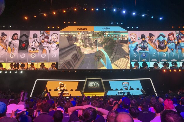In this Friday, July 27, 2018 photo, fans watch the Philadelphia Fusion and London Spitfire compete in the Overwatch League Grand Finals' first night of competition at the Barclays Center in the Brooklyn borough of New York. The Overwatch League is making a grand gamble: that its deep pockets and massive infrastructure can keep it atop the esports mountain even as Fortnite comes charging for the crown. (AP Photo/Terrin Waack)