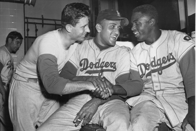 FILE - In this Sept. 29, 1951 file photo, Brooklyn Dodgers baseball player Andy Pafko, left, Don Newcomb, center, and Jackie Robinson shake hands in their dressing room after the Dodgers beat the Philadelphia Phillies 5-0, in New York. That flowing blue