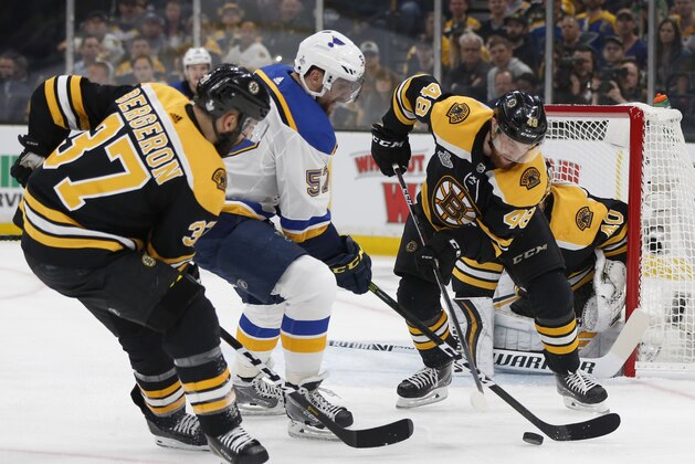 St. Louis Blues' David Perron (57) tries to move the puck between Boston Bruins' Patrice Bergeron (37) and Matt Grzelcyk (48) during the first period in Game 1 of the NHL hockey Stanley Cup Final, Monday, May 27, 2019, in Boston. (AP Photo/Michael Dwyer)