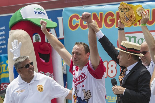 Reigning champion Joey Chestnut, center, celebrates with Master of ceremonies  George Shea, right, and Brooklyn District Attorney Eric Gonzalez, after winning the men's competition of the Nathan's Famous Fourth of July hot dog eating contest in the final seconds of the competition, Wednesday, July 4, 2018, in New York's Coney Island.  Chestnut broke his own world record by eating 74 hot dogs in 10 minutes. (AP Photo/Mary Altaffer)