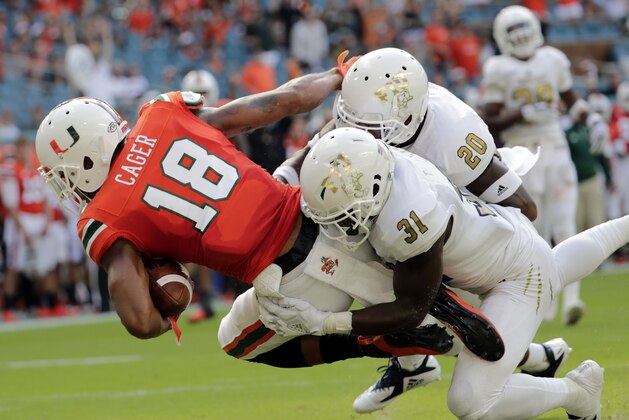 Miami wide receiver Lawrence Cager (18) scores a touchdown as FIU defensive back Tyree Johnson (31) and defensive back Emmanuel Lubin (20) defend during the first half of an NCAA college football game, Saturday, Sept. 22, 2018, in Miami Gardens, Fla. (AP Photo/Lynne Sladky)