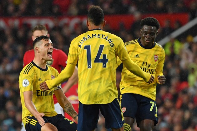 Arsenal's Gabonese striker Pierre-Emerick Aubameyang (C) celebrates with Arsenal's Swiss midfielder Granit Xhaka (L) and Arsenal's English striker Bukayo Saka (R) after scoring their first goal, decision of off-side overturned by VAR (Video Assistant referee) during the English Premier League football match between Manchester United and Arsenal at Old Trafford in Manchester, north west England, on September 30, 2019. (Photo by Paul ELLIS / AFP) / RESTRICTED TO EDITORIAL USE. No use with unauthorized audio, video, data, fixture lists, club/league logos or 'live' services. Online in-match use limited to 120 images. An additional 40 images may be used in extra time. No video emulation. Social media in-match use limited to 120 images. An additional 40 images may be used in extra time. No use in betting publications, games or single club/league/player publications. /         (Photo credit should read PAUL ELLIS/AFP/Getty Images)