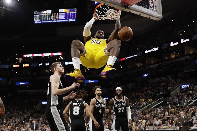 Los Angeles Lakers forward LeBron James (23) hangs on the rim as he scores against the San Antonio Spurs during the first half of an NBA basketball game, in San Antonio, Monday, Nov. 25, 2019. (AP Photo/Eric Gay)