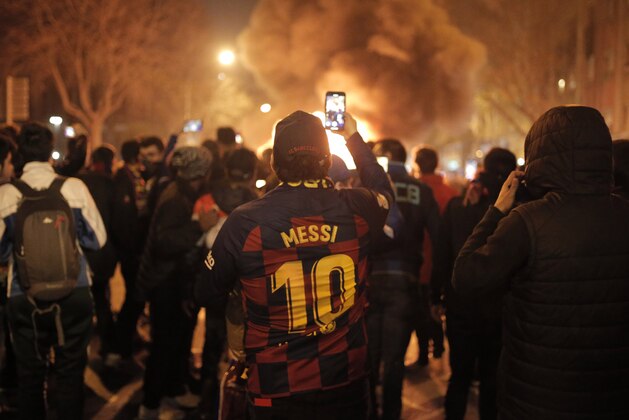 A man takes photos of fires that burn toward the end of a Catalan pro-independence protest outside the Camp Nou stadium in Barcelona, Spain, Wednesday, Dec. 18, 2019. Thousands of Catalan separatists protested around and inside Barcelona's Camp Nou Stadium during Wednesday's match against fierce rival Real Madrid. (AP Photo/Joan Mateu)