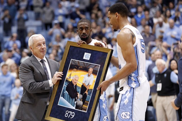 North Carolina coach Roy Williams, left, is presented with a photograph of himself with Dean Smith by players Brandon Robinson, center, and Garrison Brooks, right, following an NCAA college basketball game against Yale in Chapel Hill, N.C., Monday, Dec. 30, 2019. (AP Photo/Gerry Broome)