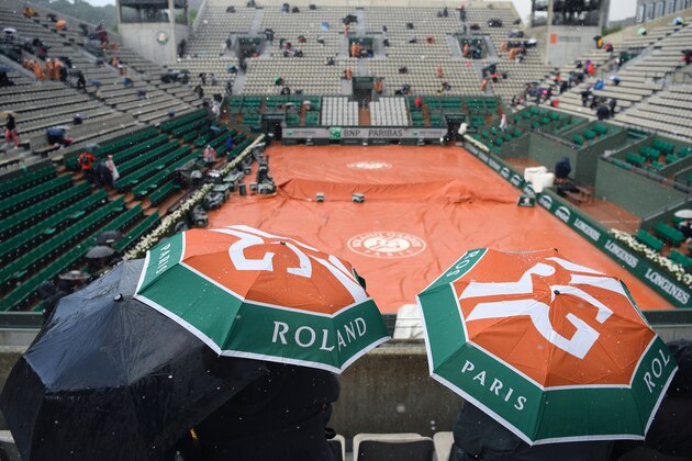 People hold umbrellas at the Suzanne Lenglen court after it was covered with a tarp when rain stopped play at the Roland Garros 2017 French Open on June 6, 2017 in Paris.  / AFP PHOTO / GABRIEL BOUYS        (Photo credit should read GABRIEL BOUYS/AFP via Getty Images)