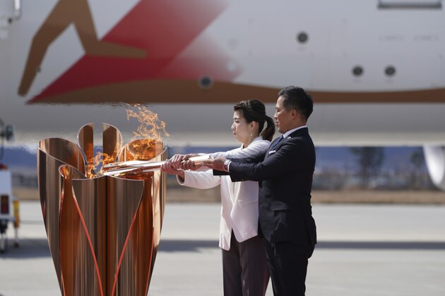 Three-time Olympic gold medalists Tadahiro Nomura, right, and Saori Yoshida light the torch during Olympic Flame Arrival Ceremony at Japan Air Self-Defense Force Matsushima Base in Higashimatsushima in Miyagi Prefecture, north of Tokyo Friday, March 20, 2020. The Olympic flame from Greece is set to arrive in Japan even as the opening of the the Tokyo Games in four months is in doubt with more voices suggesting the games should to be postponed or canceled because of the worldwide virus pandemic. (AP Photo/Eugene Hoshiko)